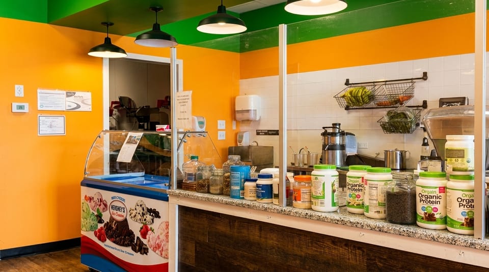A vibrant juice bar interior with an ice cream freezer, protein powders, and fresh produce.
