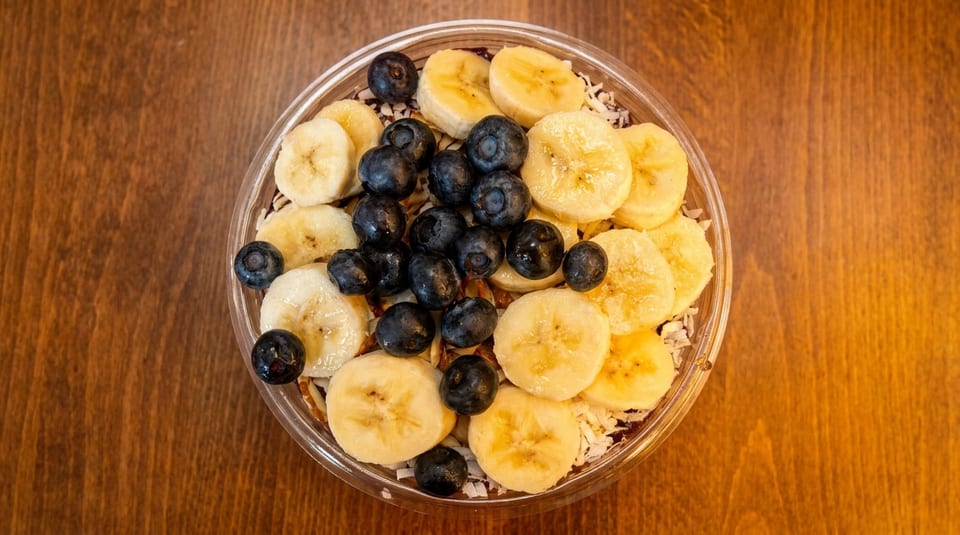 Overhead view of an acai bowl topped with sliced bananas, blueberries, and shredded coconut.